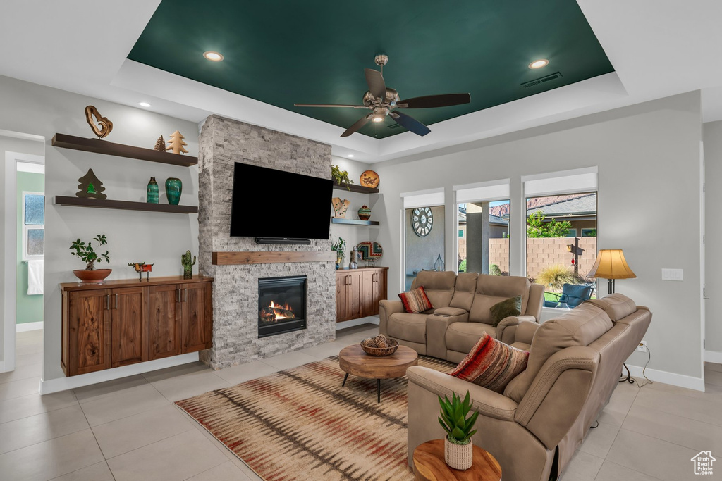 Living room with a raised ceiling, baseboards, light tile patterned flooring, ceiling fan, and a fireplace