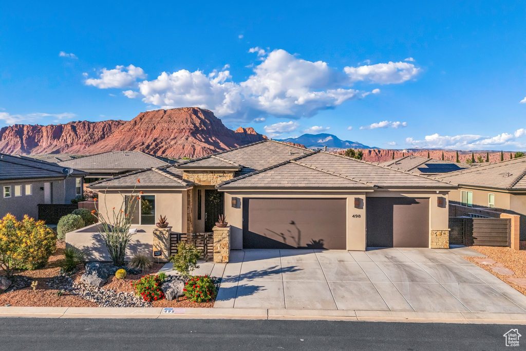Ranch-style home featuring a garage, stucco siding, driveway, a mountain view, and stone siding