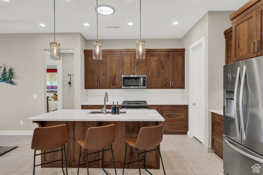 Kitchen with stainless steel appliances, a sink, light countertops, a kitchen bar, and recessed lighting