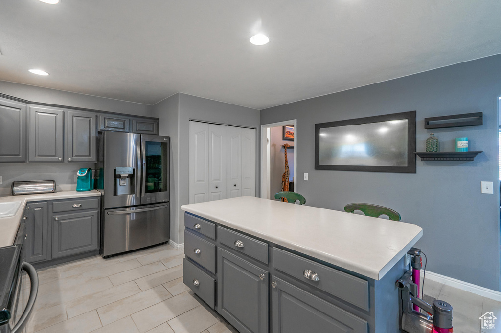 Kitchen featuring stainless steel fridge with ice dispenser, gray cabinets, range, light countertops, and baseboards