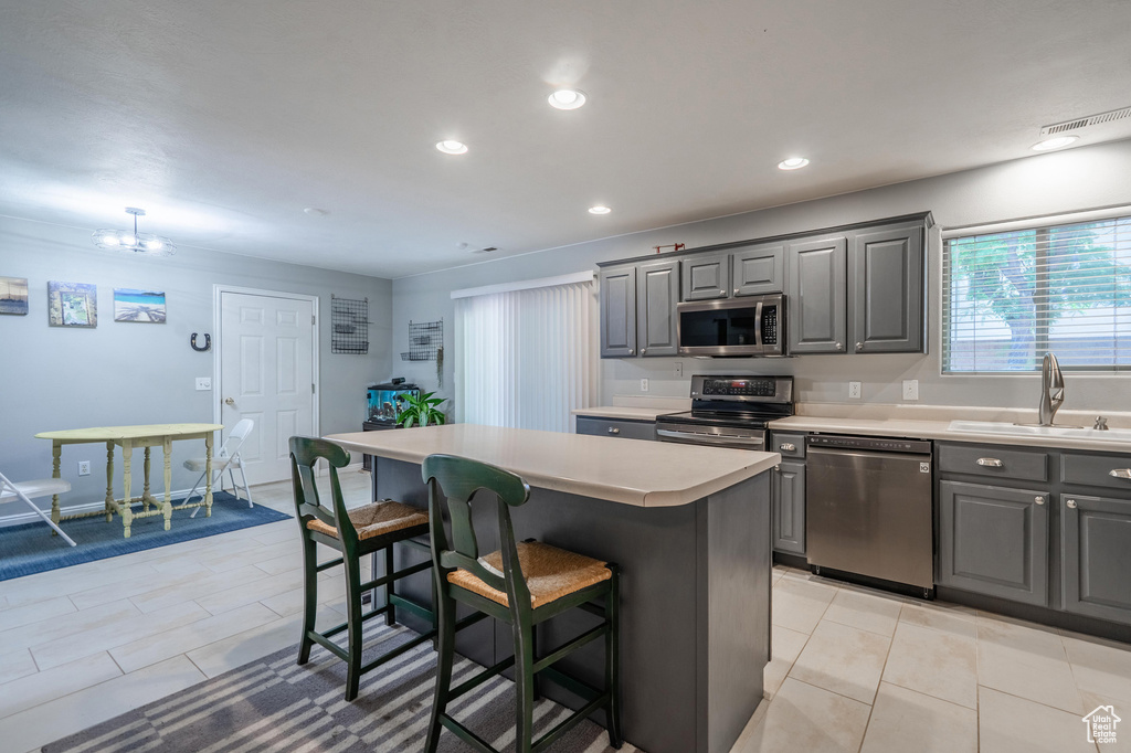 Kitchen with appliances with stainless steel finishes, gray cabinets, a sink, a breakfast bar area, and a center island
