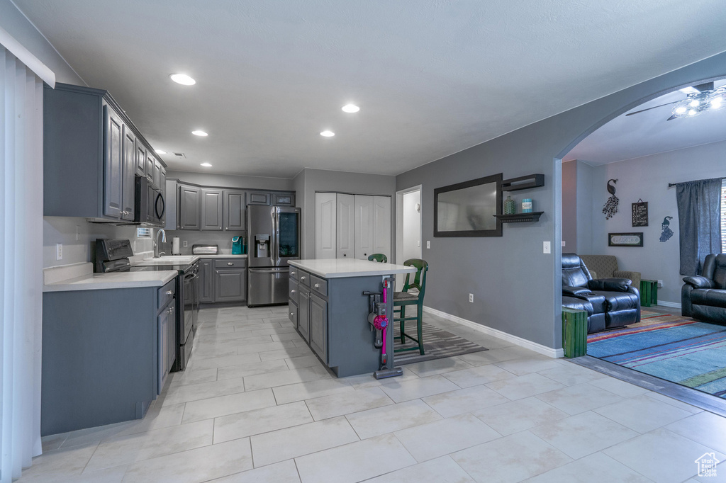 Kitchen with black appliances, gray cabinetry, arched walkways, light countertops, and recessed lighting