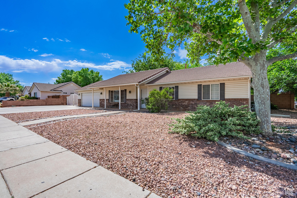 Ranch-style house featuring brick siding, driveway, a tiled roof, an attached garage, and fence