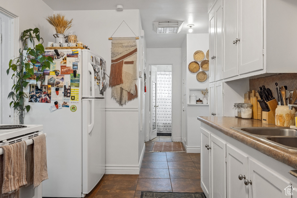 Kitchen with white appliances, white cabinetry, a sink, dark tile patterned flooring, and baseboards
