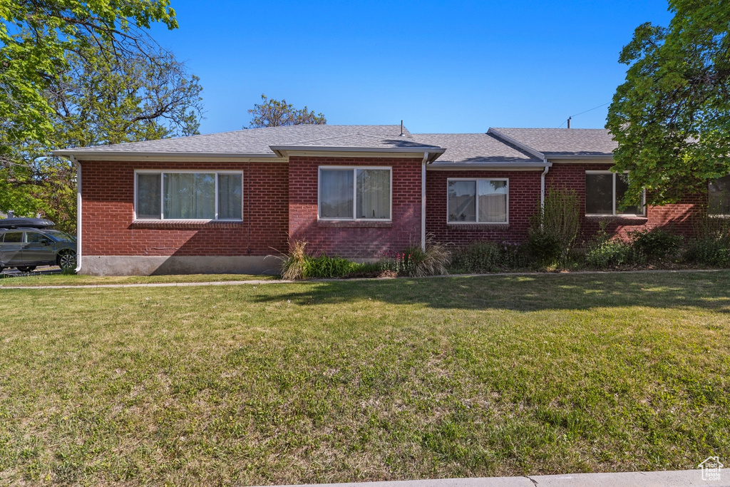 View of front of house with a front yard, brick siding, and roof with shingles