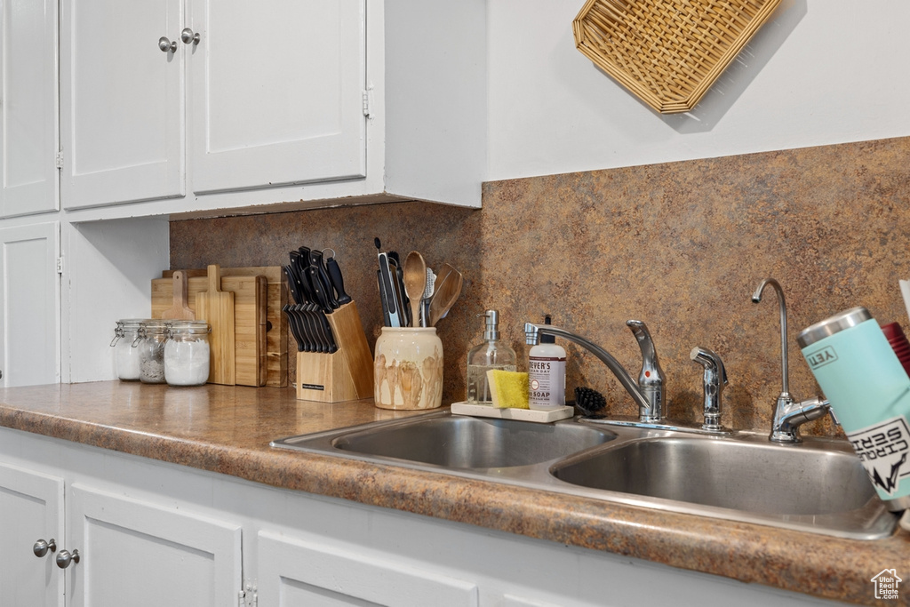 Kitchen view of white cabinetry, backsplash, a sink, and dark countertops