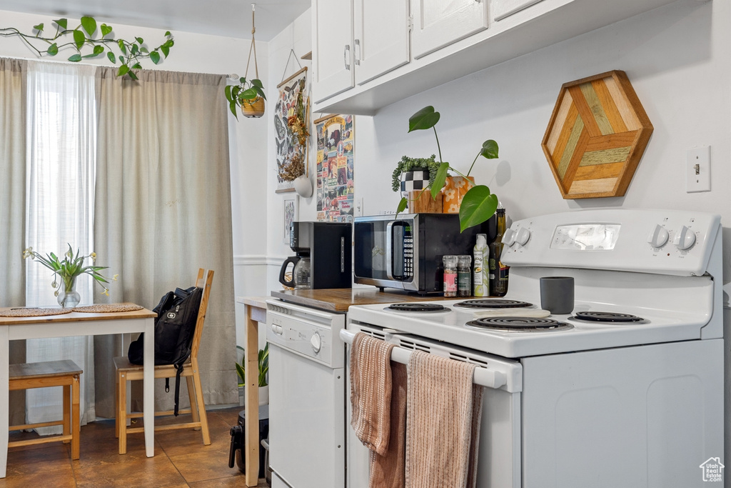 Kitchen with white electric stove, stainless steel microwave, and white cabinets