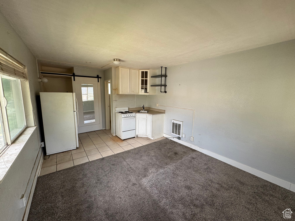 Kitchen featuring white appliances, open shelves, a sink, a barn door, and light tile patterned floors