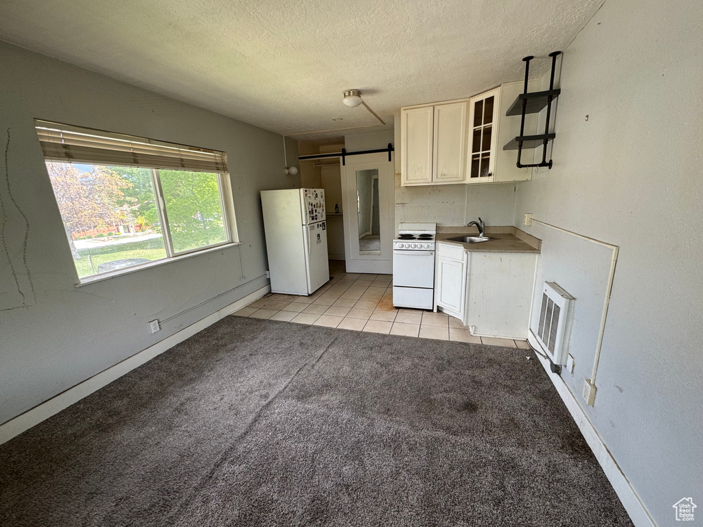 Kitchen with white appliances, a sink, a textured ceiling, glass insert cabinets, and light carpet