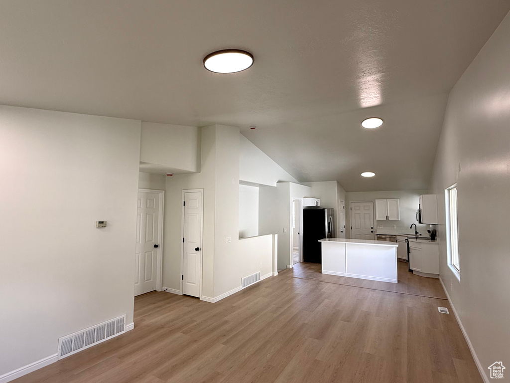Kitchen featuring freestanding refrigerator, vaulted ceiling, light wood-style floors, white cabinetry, and a kitchen island