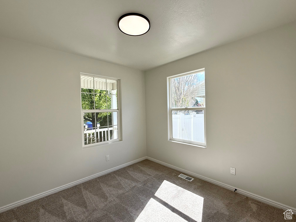 Empty room featuring plenty of natural light, dark colored carpet, and baseboards