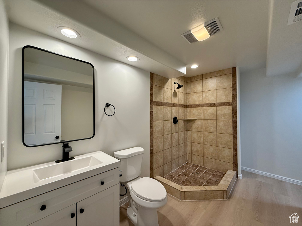 Full bathroom with toilet, a tile shower, wood finished floors, vanity, and recessed lighting