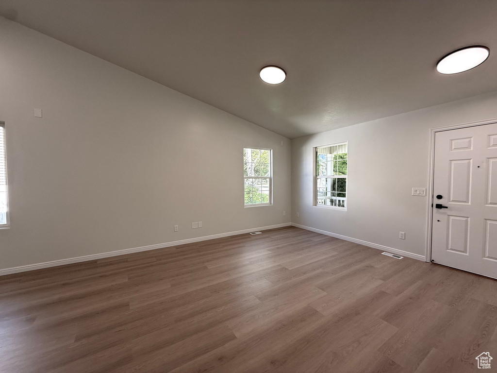 Unfurnished room with wood finished floors, baseboards, and lofted ceiling