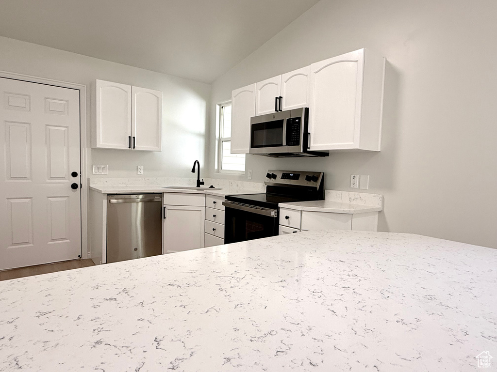 Kitchen featuring stainless steel appliances, a sink, vaulted ceiling, white cabinets, and light stone countertops