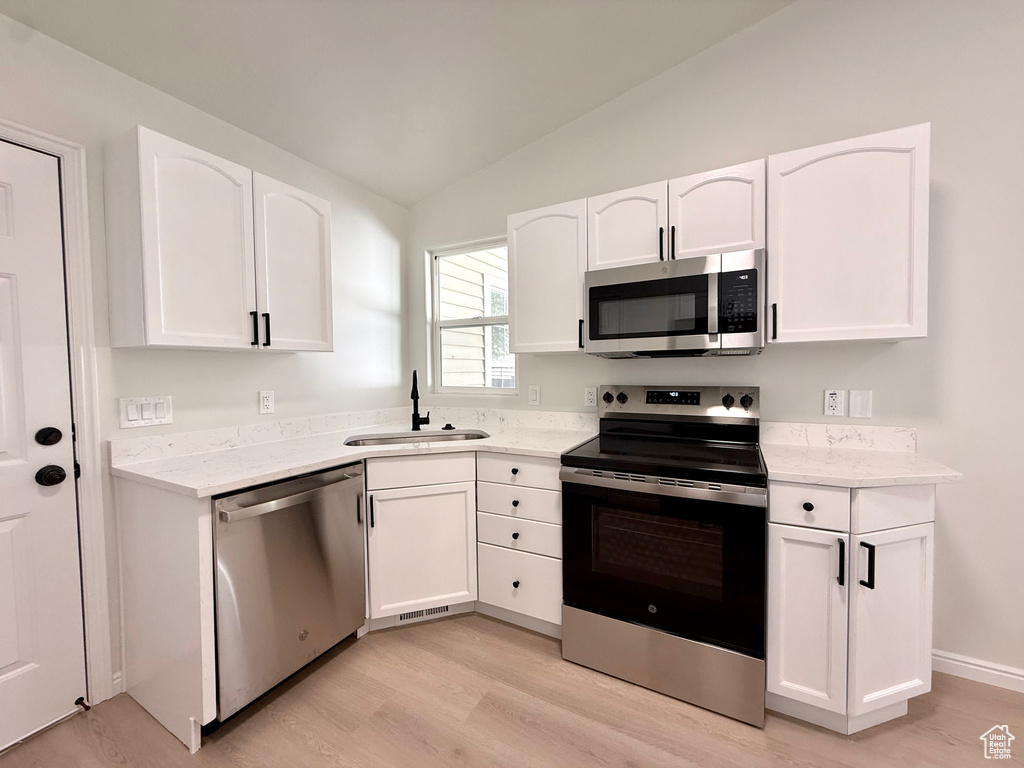Kitchen featuring stainless steel appliances, a sink, light wood-style floors, vaulted ceiling, and white cabinetry