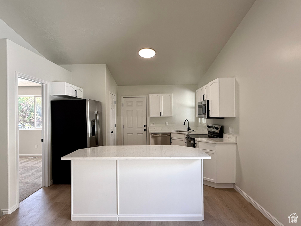 Kitchen featuring stainless steel appliances, a sink, light wood-style flooring, baseboards, and vaulted ceiling