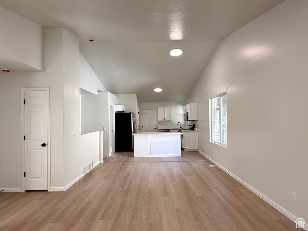 Kitchen with freestanding refrigerator, light wood finished floors, white cabinetry, high vaulted ceiling, and light countertops