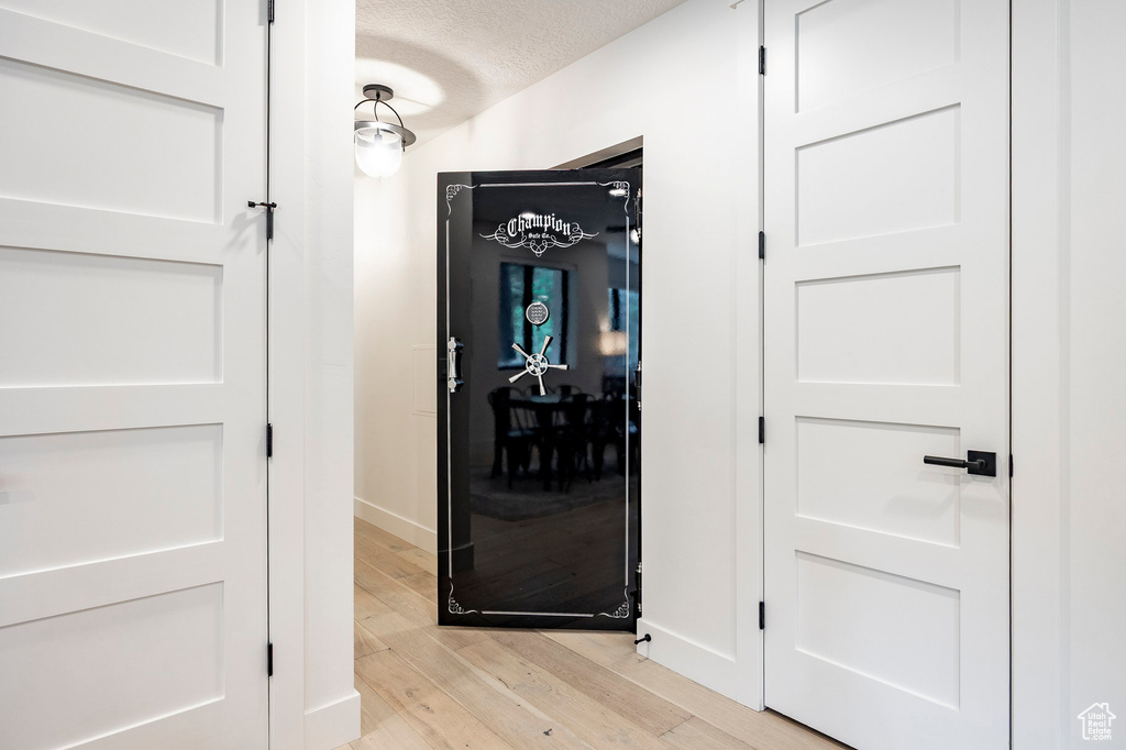 Corridor with light wood-style flooring, baseboards, and a textured ceiling