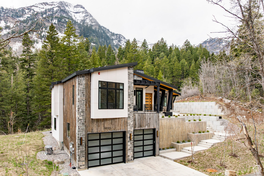 View of outdoor structure with a mountain view, driveway, stairway, an attached garage, and a view of trees