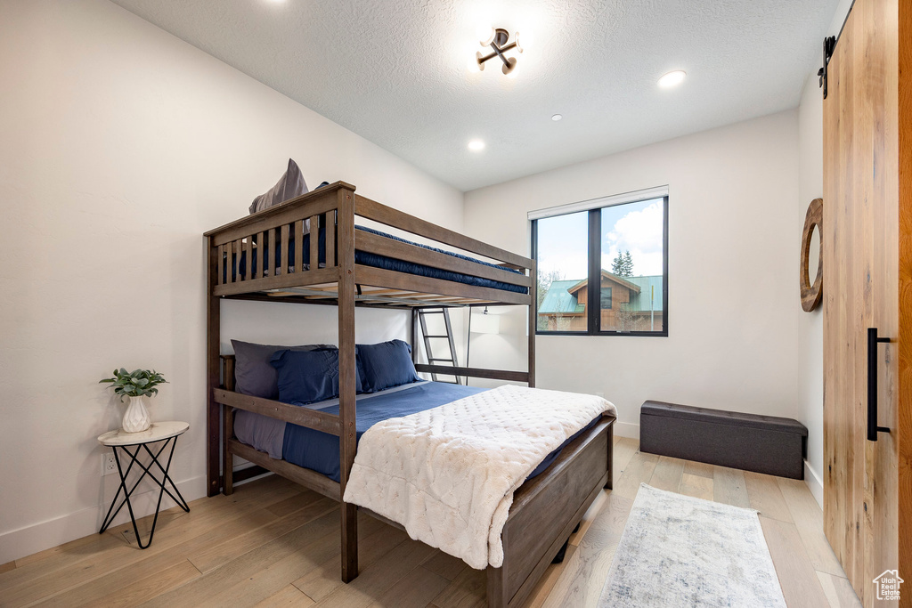 Bedroom with light wood finished floors, baseboards, recessed lighting, and a textured ceiling