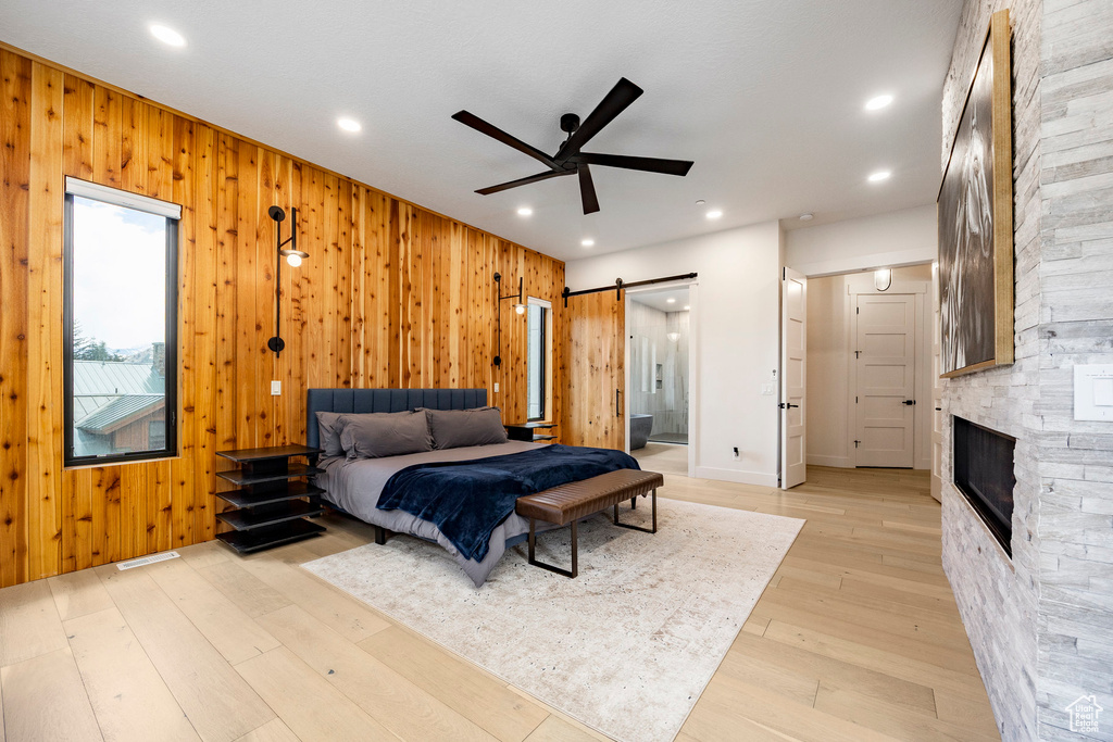 Bedroom with a barn door, wooden walls, light wood-type flooring, connected bathroom, and recessed lighting