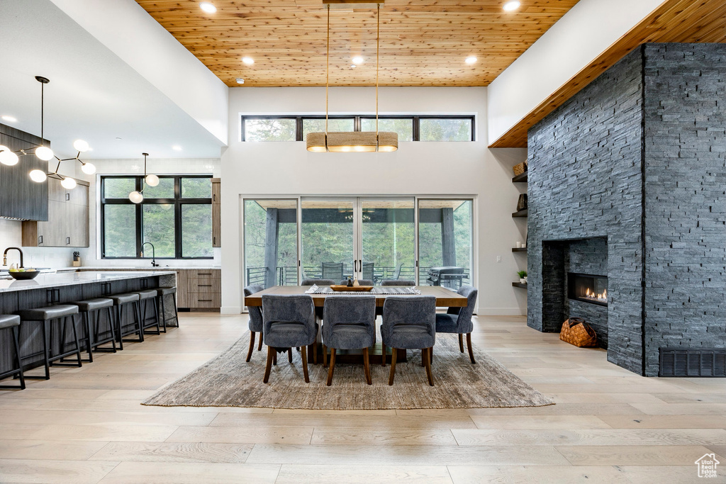Dining area with wooden ceiling, light wood-style flooring, recessed lighting, a high ceiling, and a fireplace