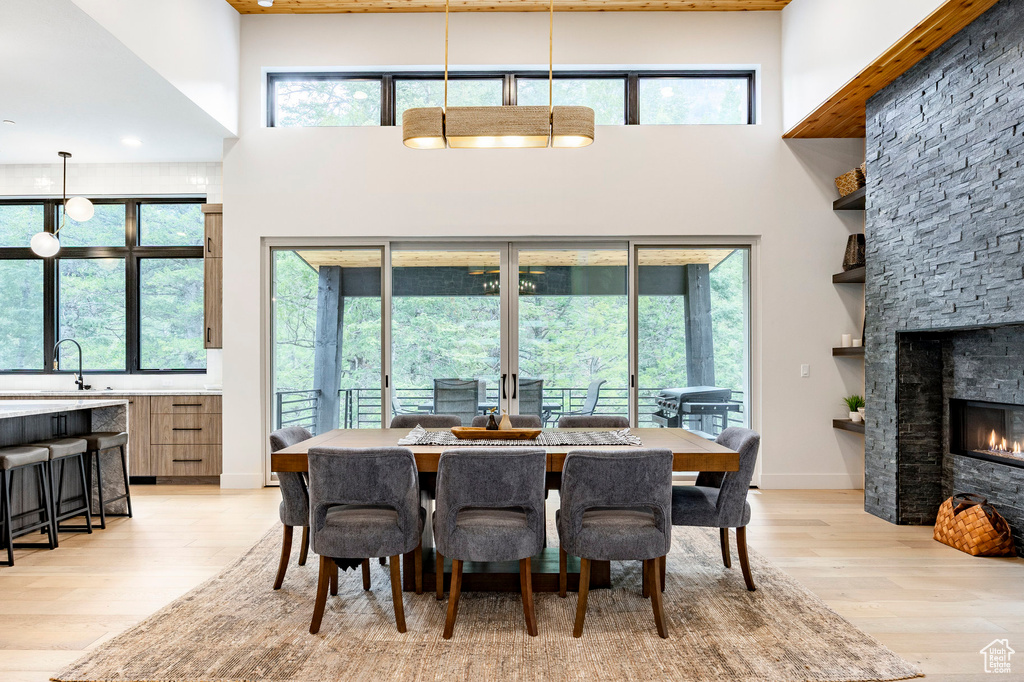 Dining area featuring a towering ceiling, light wood-type flooring, healthy amount of natural light, and a stone fireplace