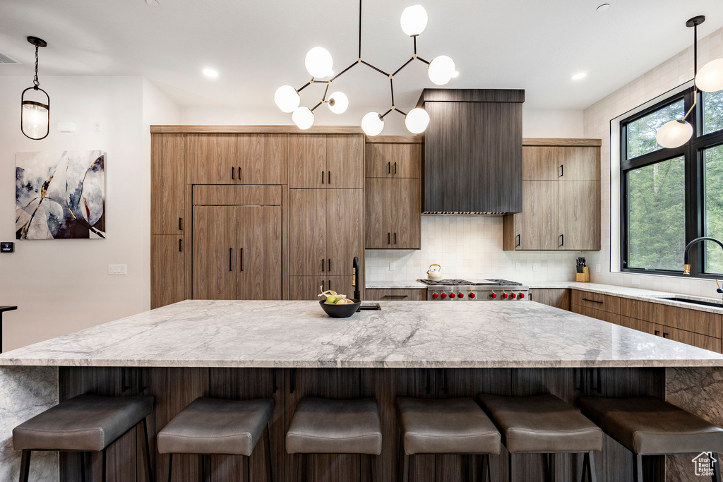 Kitchen featuring a kitchen bar, tasteful backsplash, decorative light fixtures, a large island, and a sink