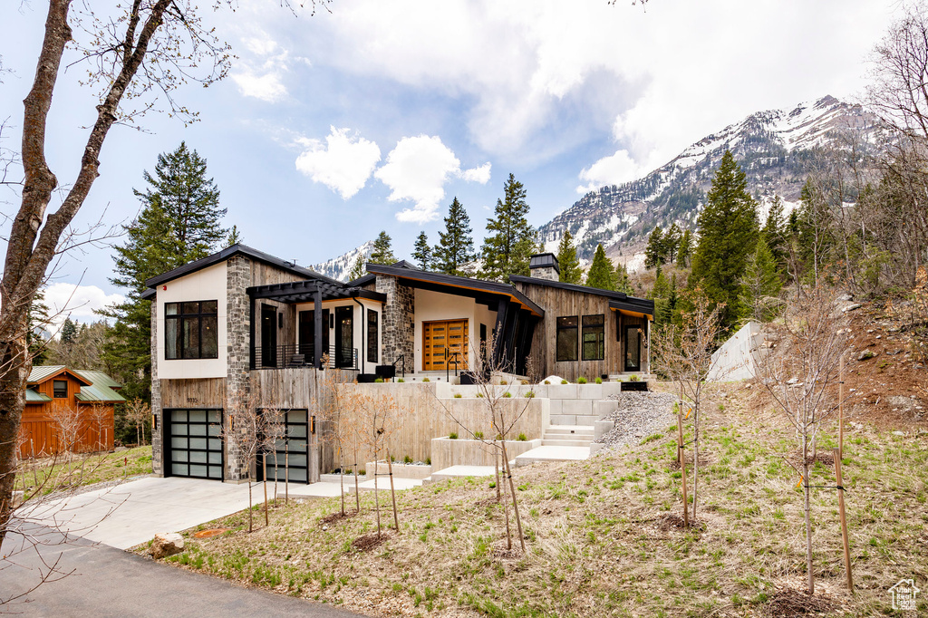 Contemporary home featuring stone siding, concrete driveway, a mountain view, a chimney, and an attached garage
