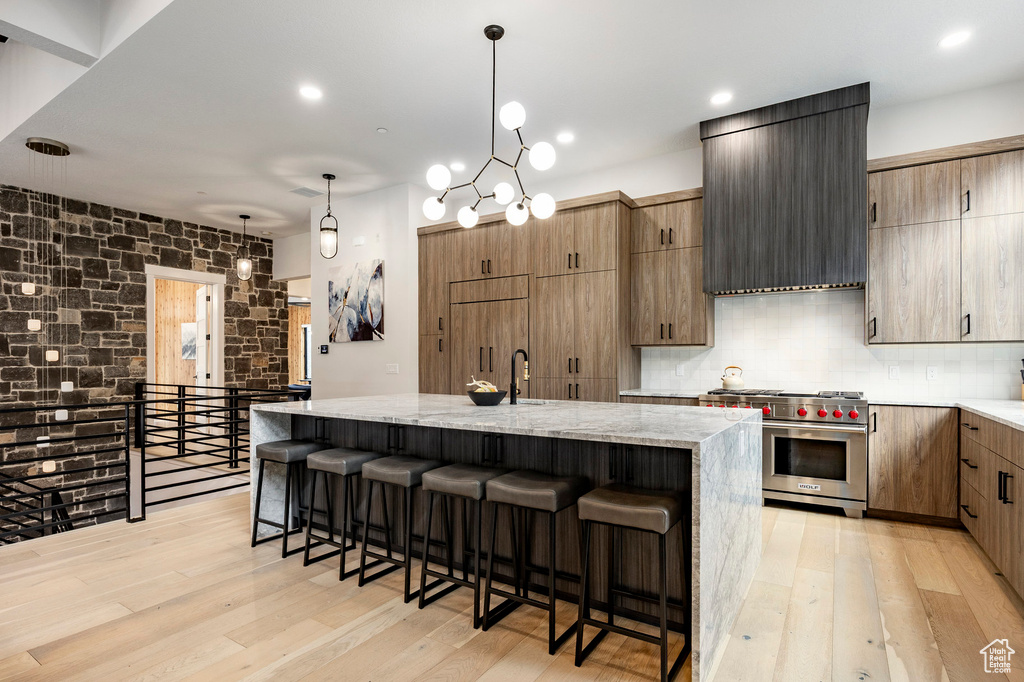 Kitchen with premium stove, a kitchen bar, light wood-type flooring, and light stone counters