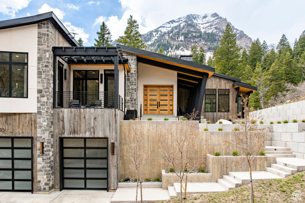 Modern home with stone siding, a mountain view, an attached garage, driveway, and a balcony