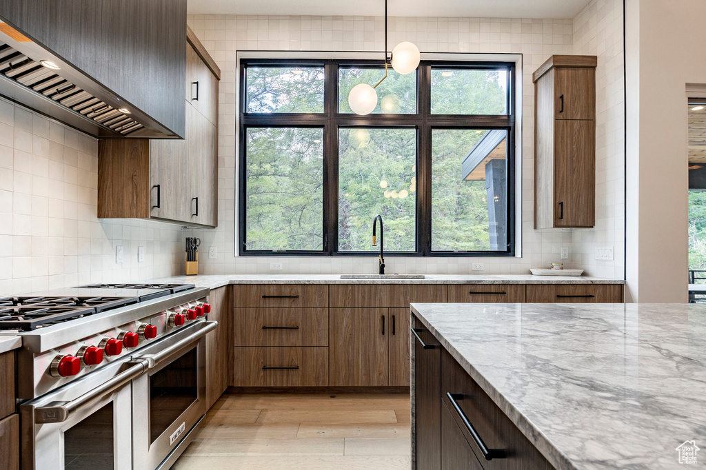 Kitchen with double oven range, custom exhaust hood, a sink, light wood-type flooring, and decorative backsplash