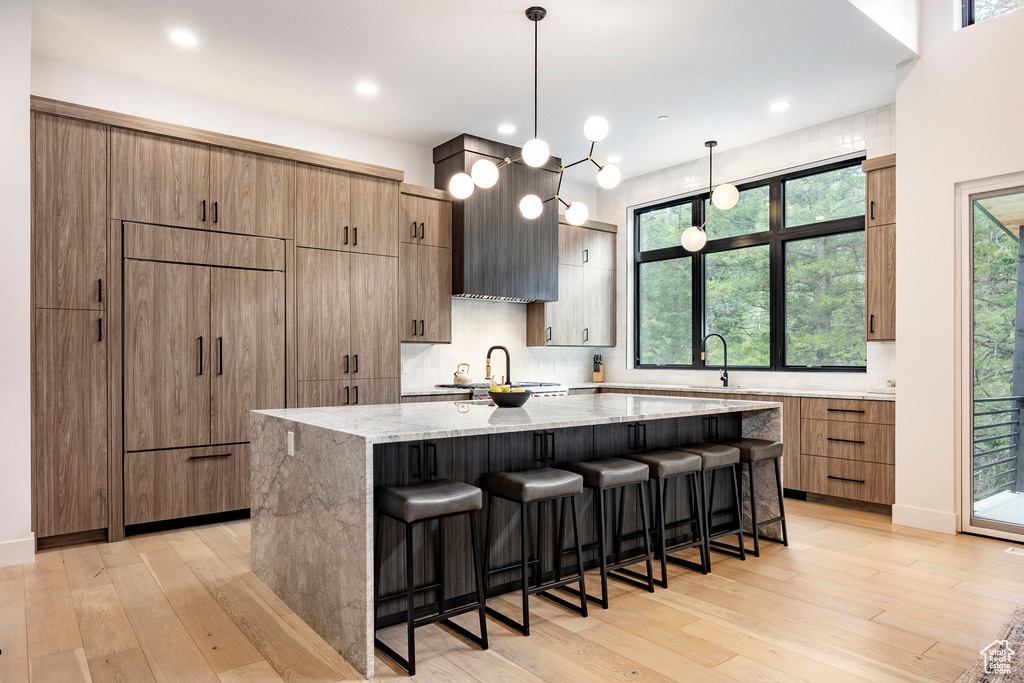 Kitchen featuring a large island, light stone counters, light wood-style flooring, decorative backsplash, and recessed lighting