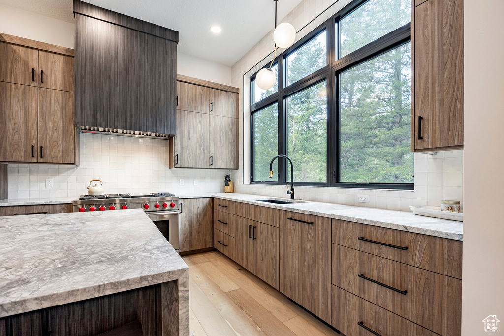 Kitchen featuring high end stainless steel range, a sink, custom range hood, light wood finished floors, and decorative backsplash