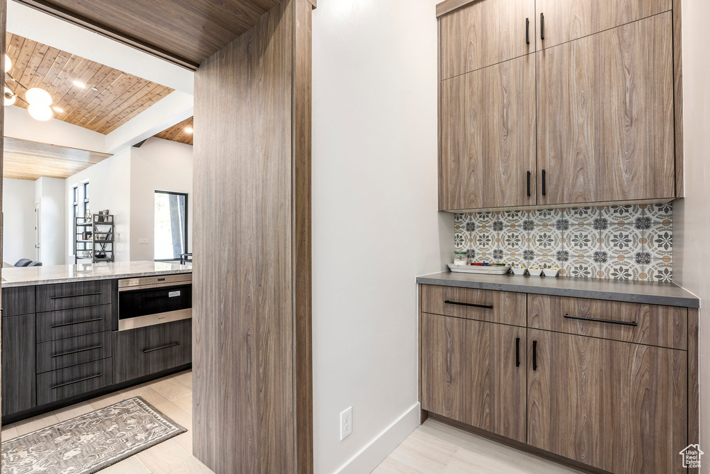 Bar area with wooden ceiling, tasteful backsplash, baseboards, and light wood-type flooring