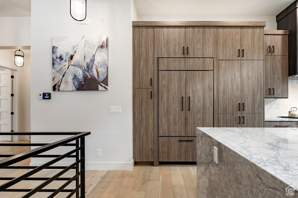 Kitchen featuring light stone counters, light wood-style floors, tasteful backsplash, baseboards, and modern cabinets