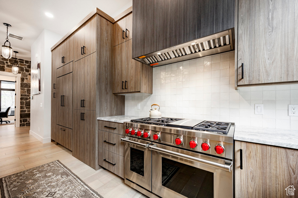 Kitchen with double oven range, wall chimney range hood, tasteful backsplash, and light wood-type flooring