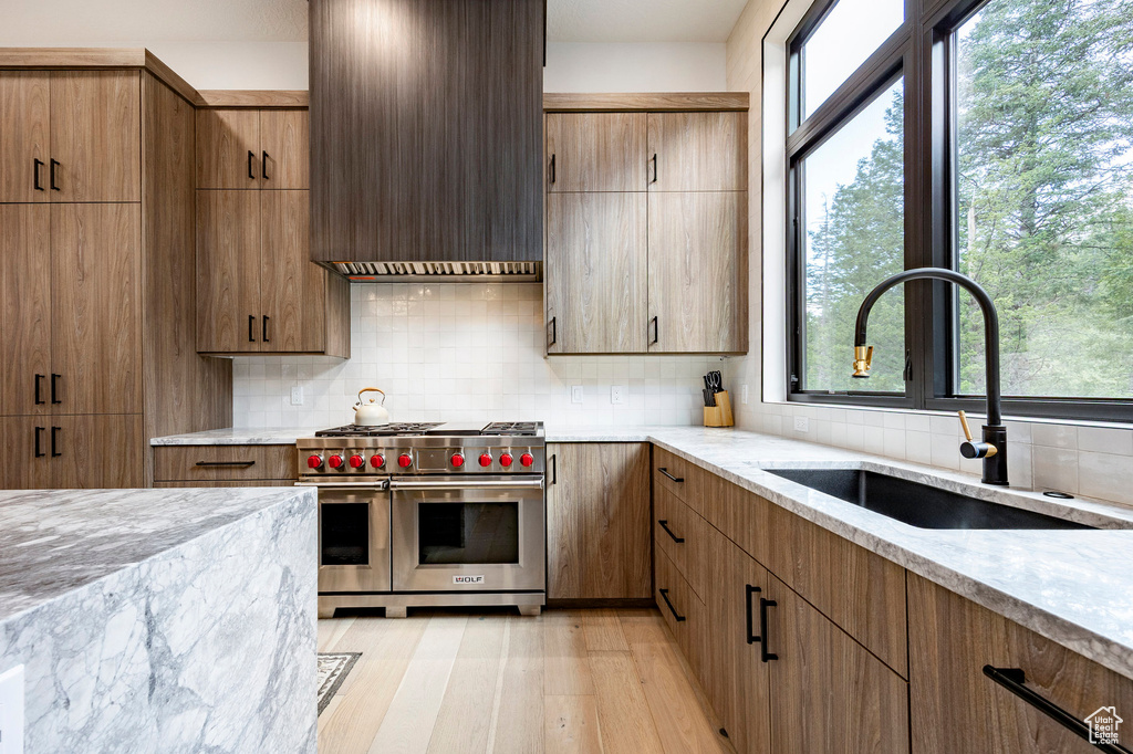 Kitchen featuring double oven range, a sink, light stone countertops, backsplash, and light wood finished floors