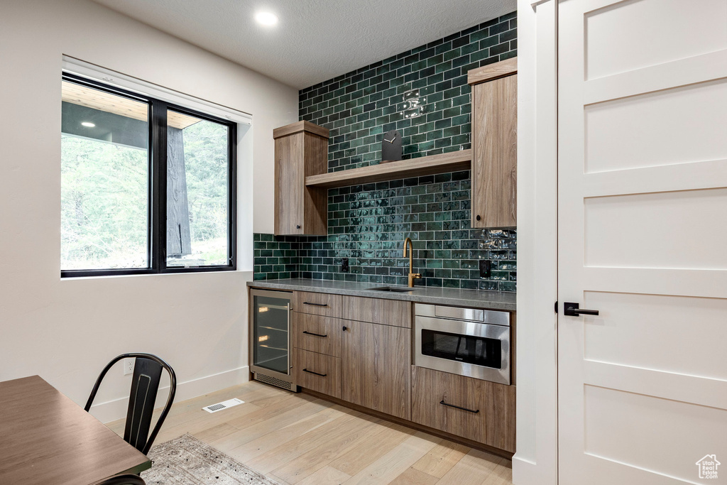 Kitchen featuring beverage cooler, a sink, open shelves, backsplash, and light wood finished floors
