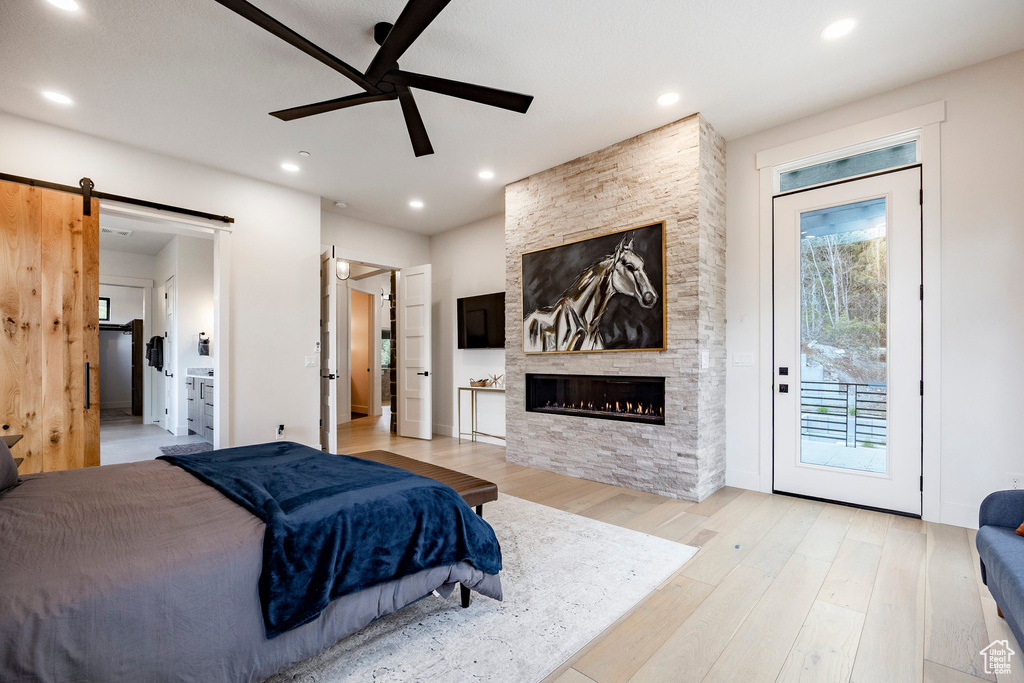 Bedroom featuring a barn door, a stone fireplace, access to outside, wood finished floors, and recessed lighting