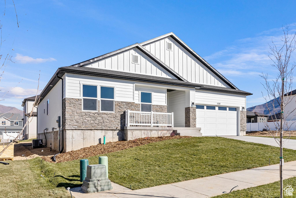 View of front facade with driveway, an attached garage, a porch, board and batten siding, and stone siding