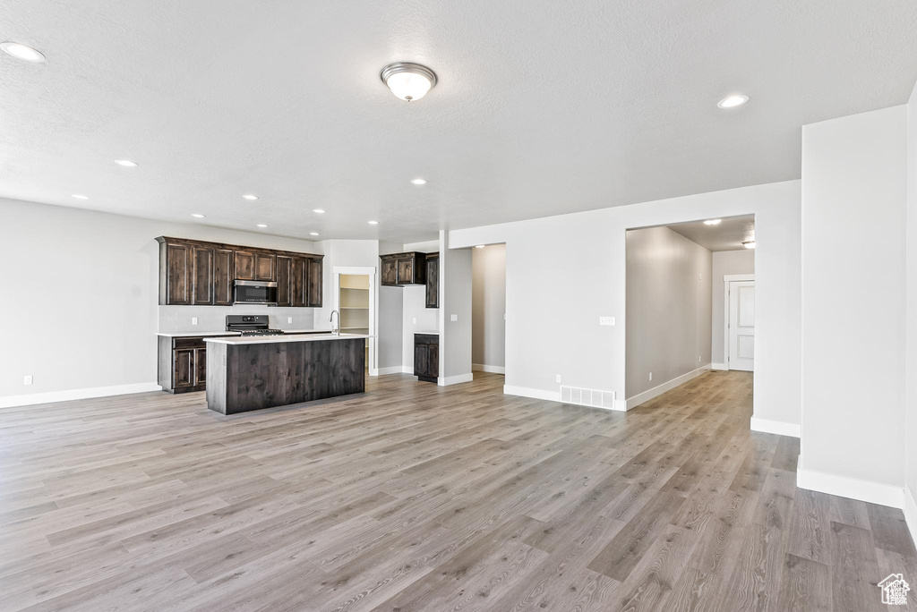 Kitchen with open floor plan, stainless steel appliances, an island with sink, light wood-style flooring, and recessed lighting