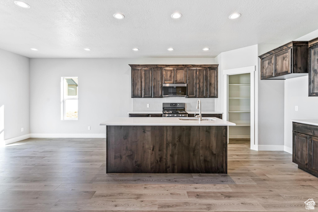 Kitchen featuring stainless steel microwave, gas range, a sink, dark brown cabinetry, and an island with sink