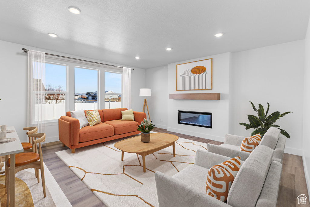 Living room featuring a glass covered fireplace, light wood finished floors, baseboards, and recessed lighting