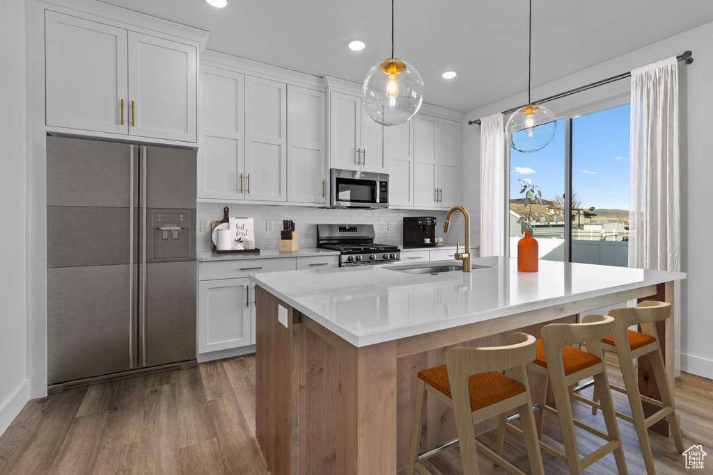 Kitchen featuring a sink, appliances with stainless steel finishes, light wood-style floors, decorative backsplash, and an island with sink