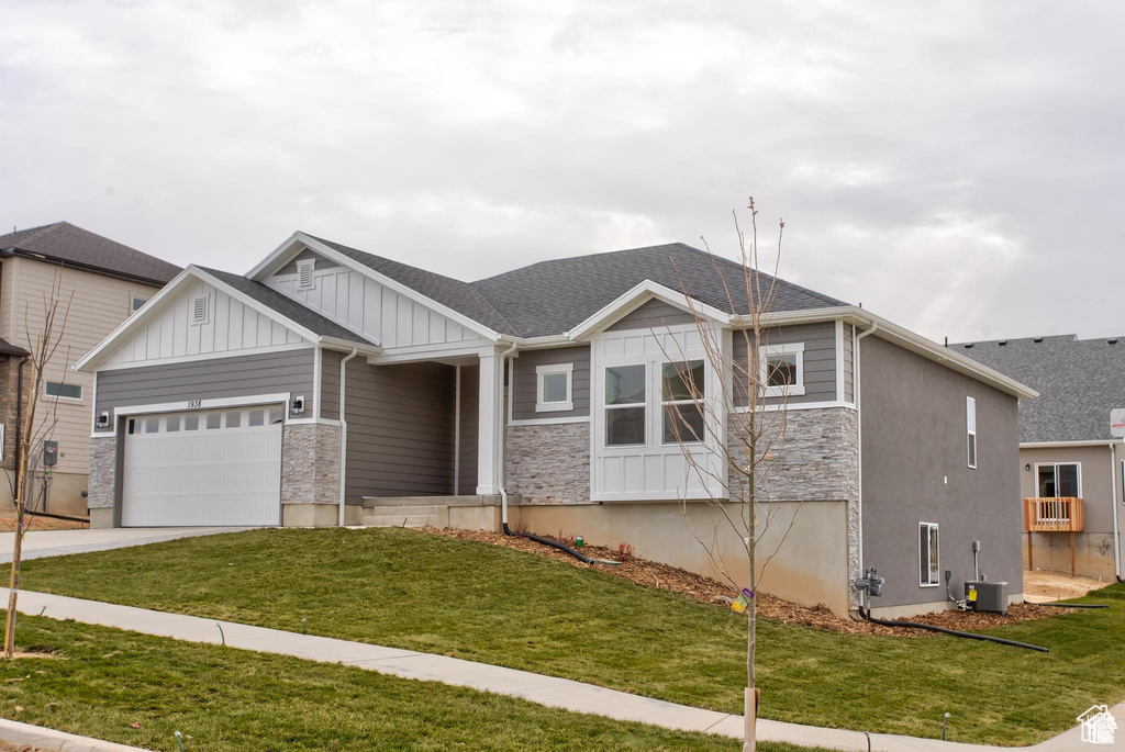 Craftsman house featuring board and batten siding, a garage, stone siding, driveway, and a front yard