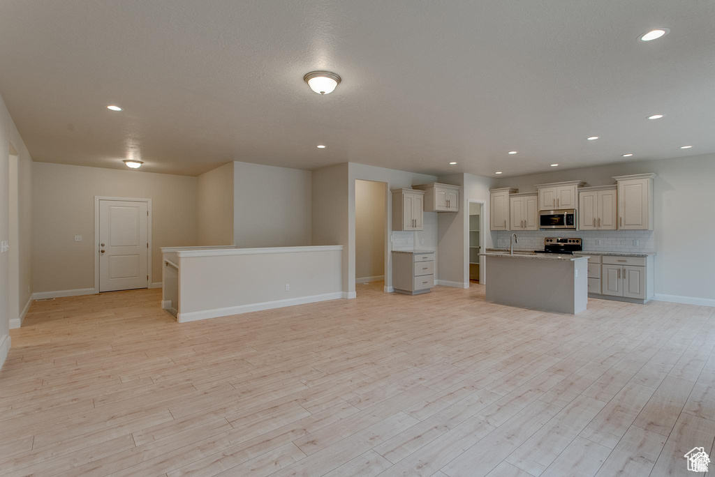 Kitchen featuring appliances with stainless steel finishes, a sink, open floor plan, backsplash, and light wood-type flooring