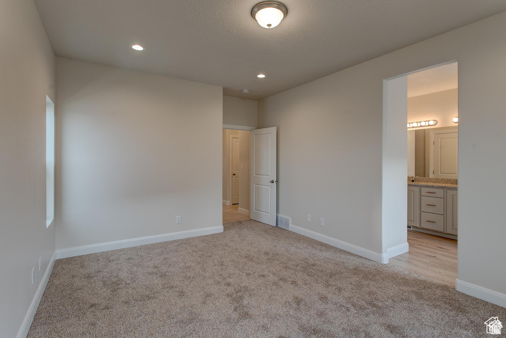Unfurnished bedroom with light carpet, baseboards, recessed lighting, and ensuite bathroom