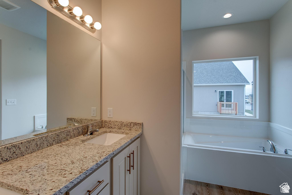 Full bath with vanity, a garden tub, recessed lighting, and wood finished floors