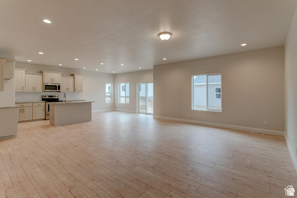 Unfurnished living room featuring a sink, baseboards, light wood-type flooring, and recessed lighting